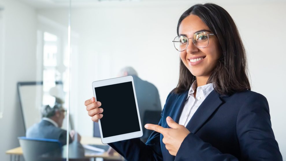 Happy confident business lady holding tablet, showing and pointing finger at blank screen, looking at camera and smiling. Copy space. Communication and advertising concept